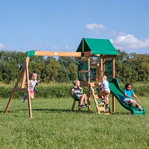 Children playing on a wooden playset with swings and a slide in a grassy field.